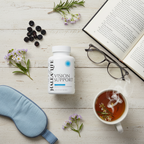 Helea Life Vision Support supplement bottle on a wooden surface with tea, flowers, and reading materials.